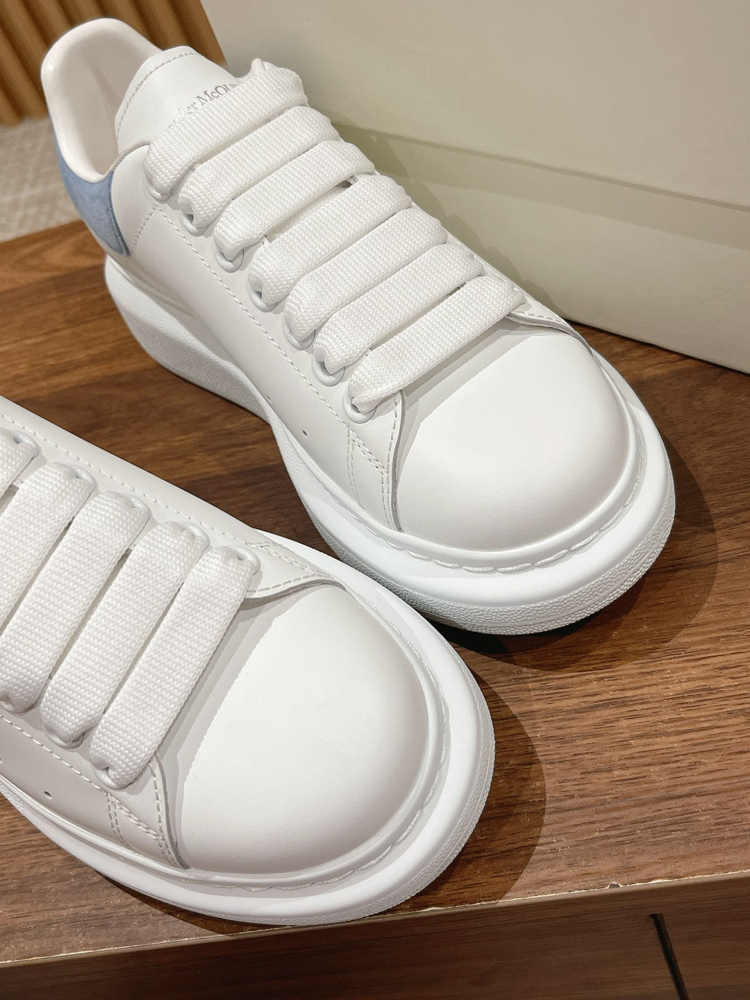 White leather lace-up sneakers with light blue heel trim and white textured rubber cupsole