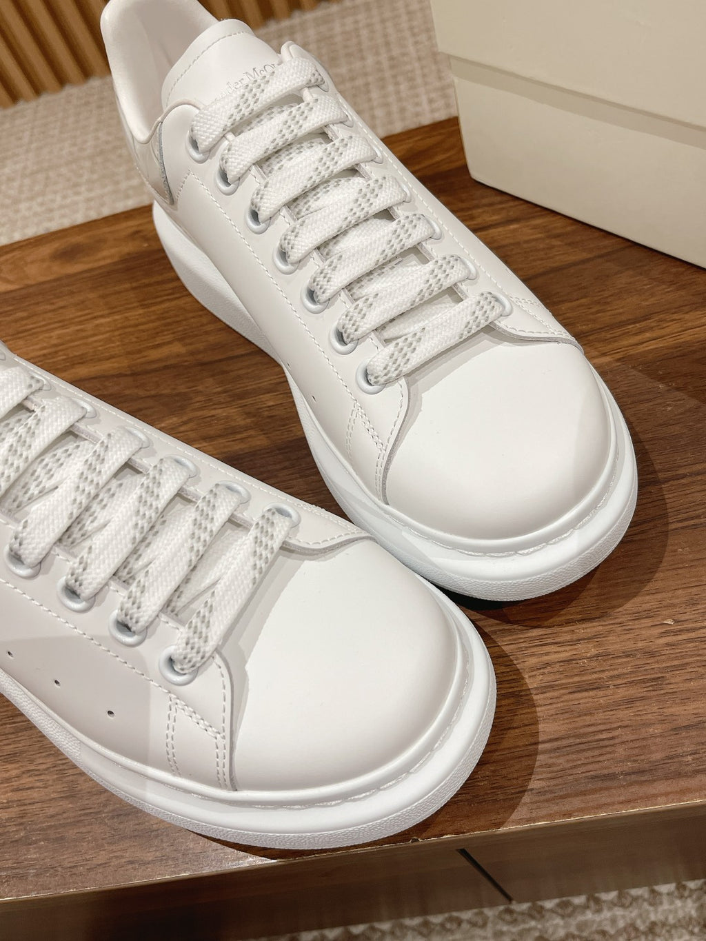White leather lace-up sneakers, angled side view, on a wooden shelf