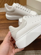 White leather lace-up sneakers held in hand, Alexander McQueen branding