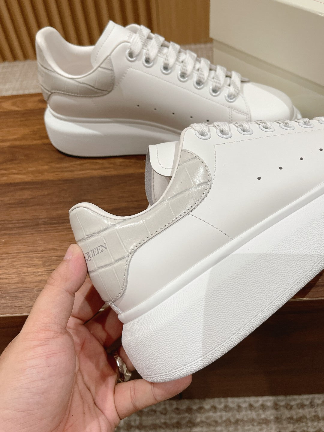 White leather lace-up sneakers held in hand, showing side logo patch detail