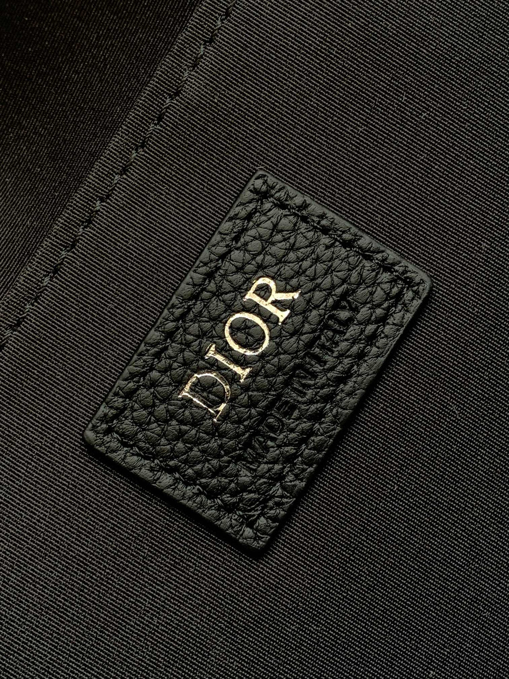 Dior logo leather patch on black interior lining of a men's Dior bag