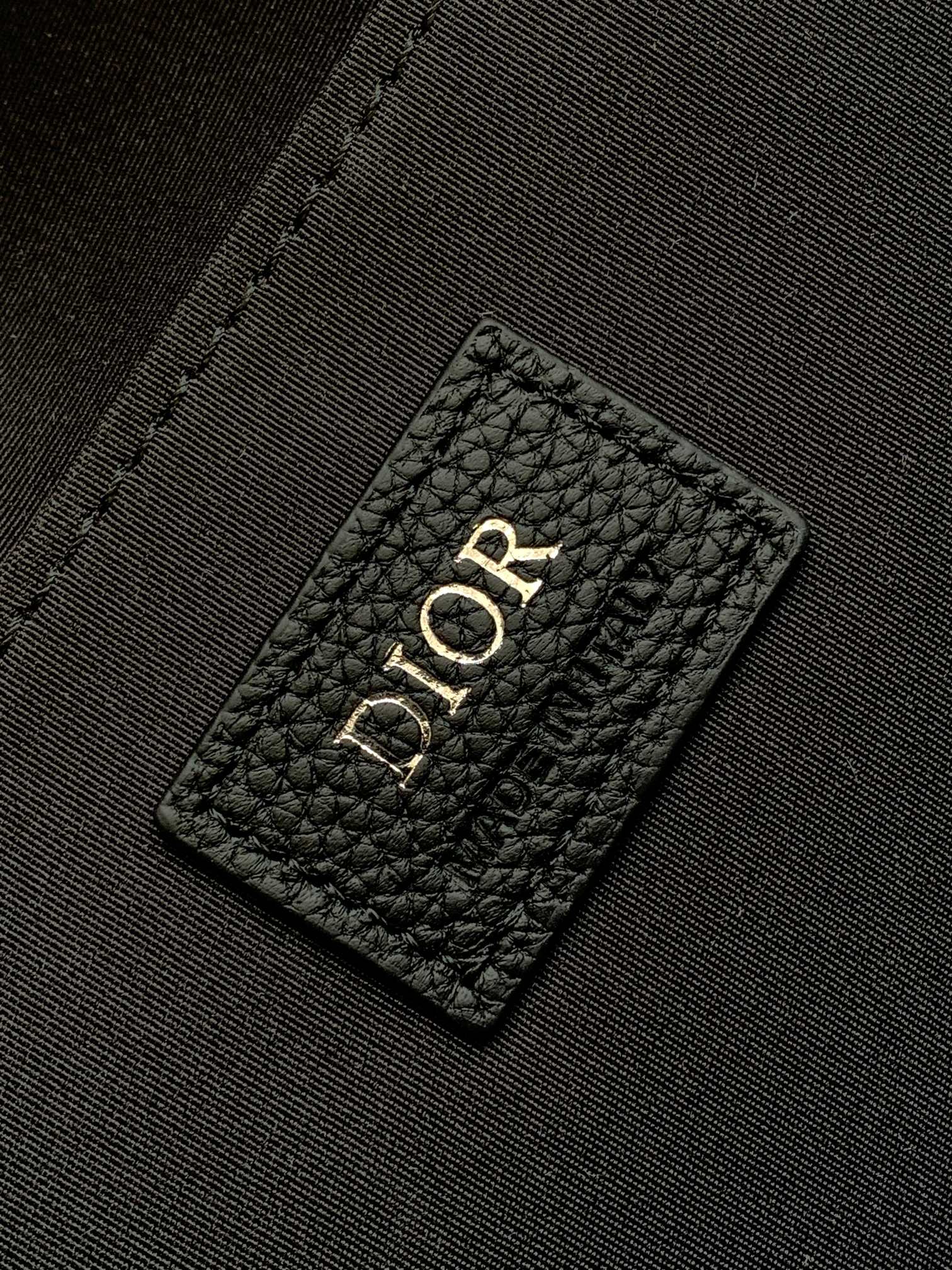 Dior logo leather patch on black interior lining of a men's Dior bag