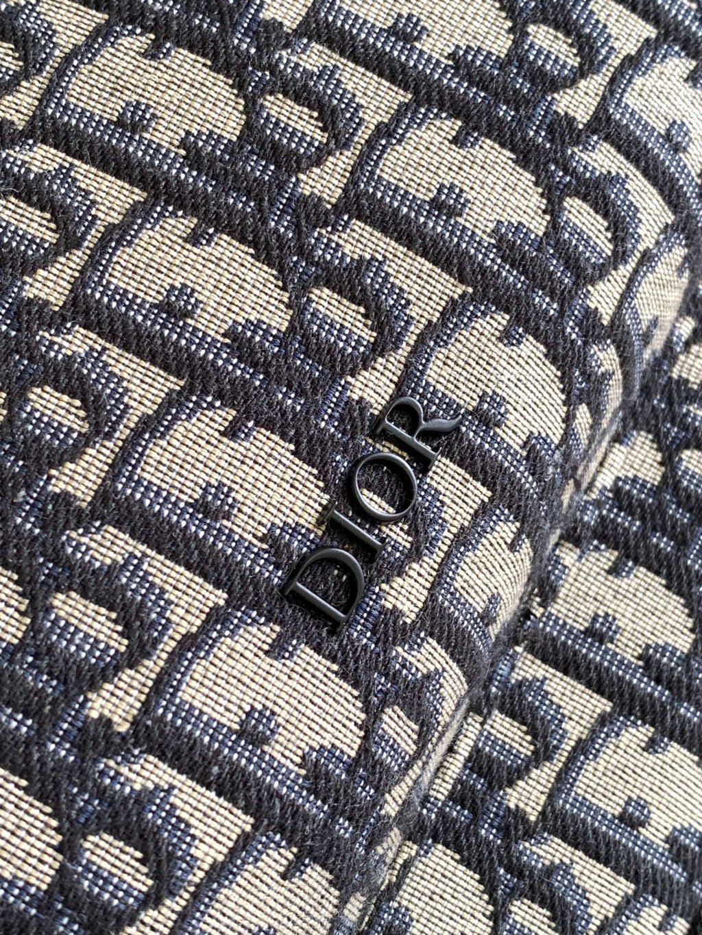 Men's Dior backpack flap showing textured Oblique pattern and metal clasp rings