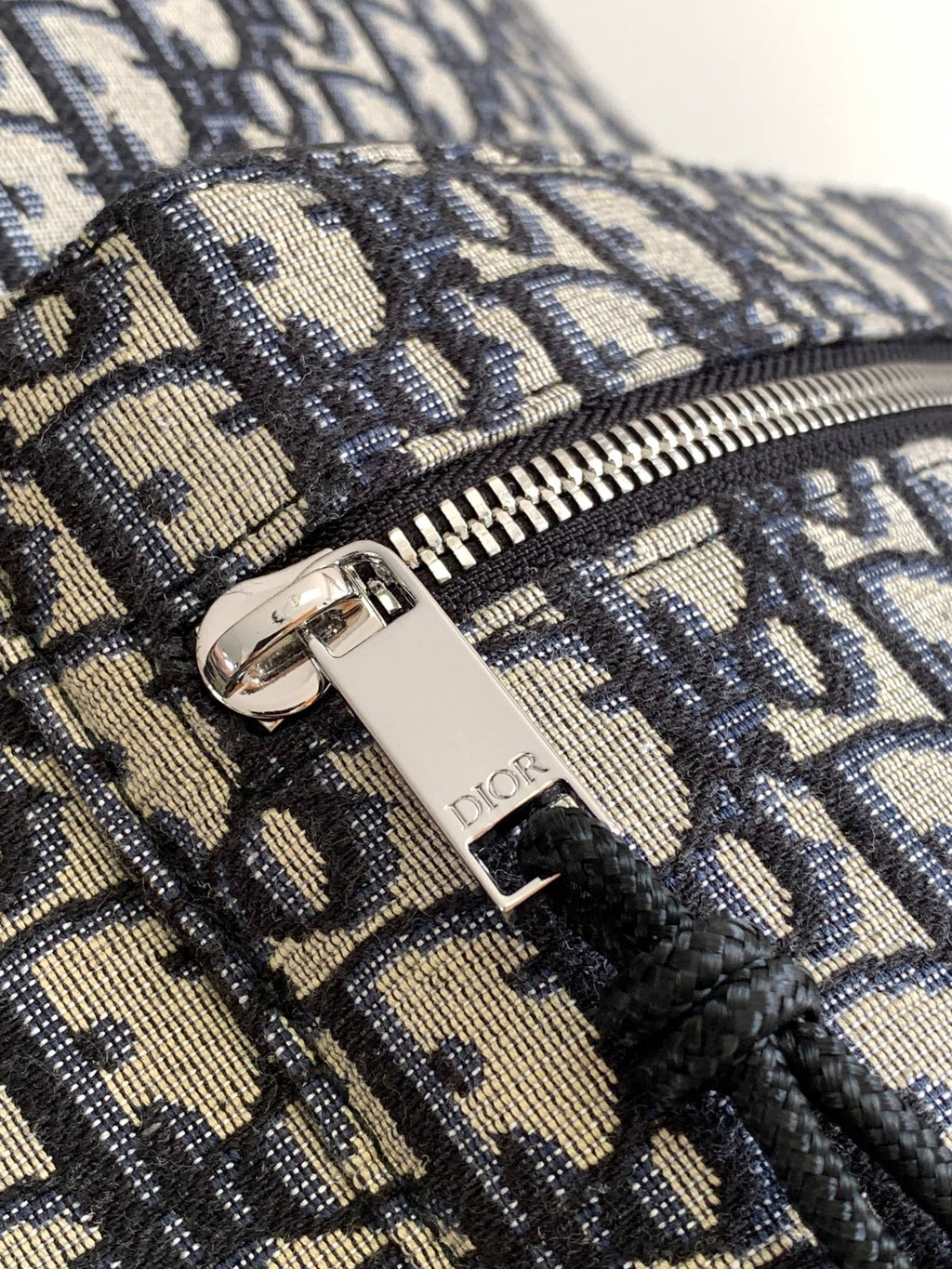 Dior men's mini backpack close-up of zipper pull with Dior logo on monogram fabric