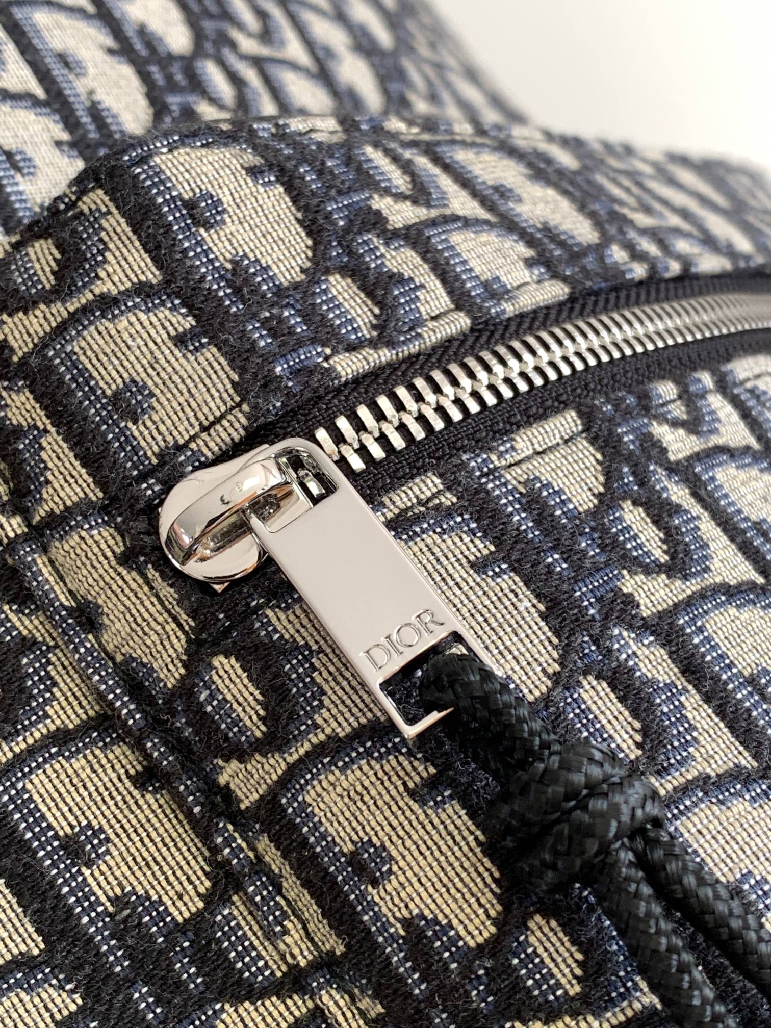 Dior men's mini backpack close-up of zipper pull with Dior logo on monogram fabric