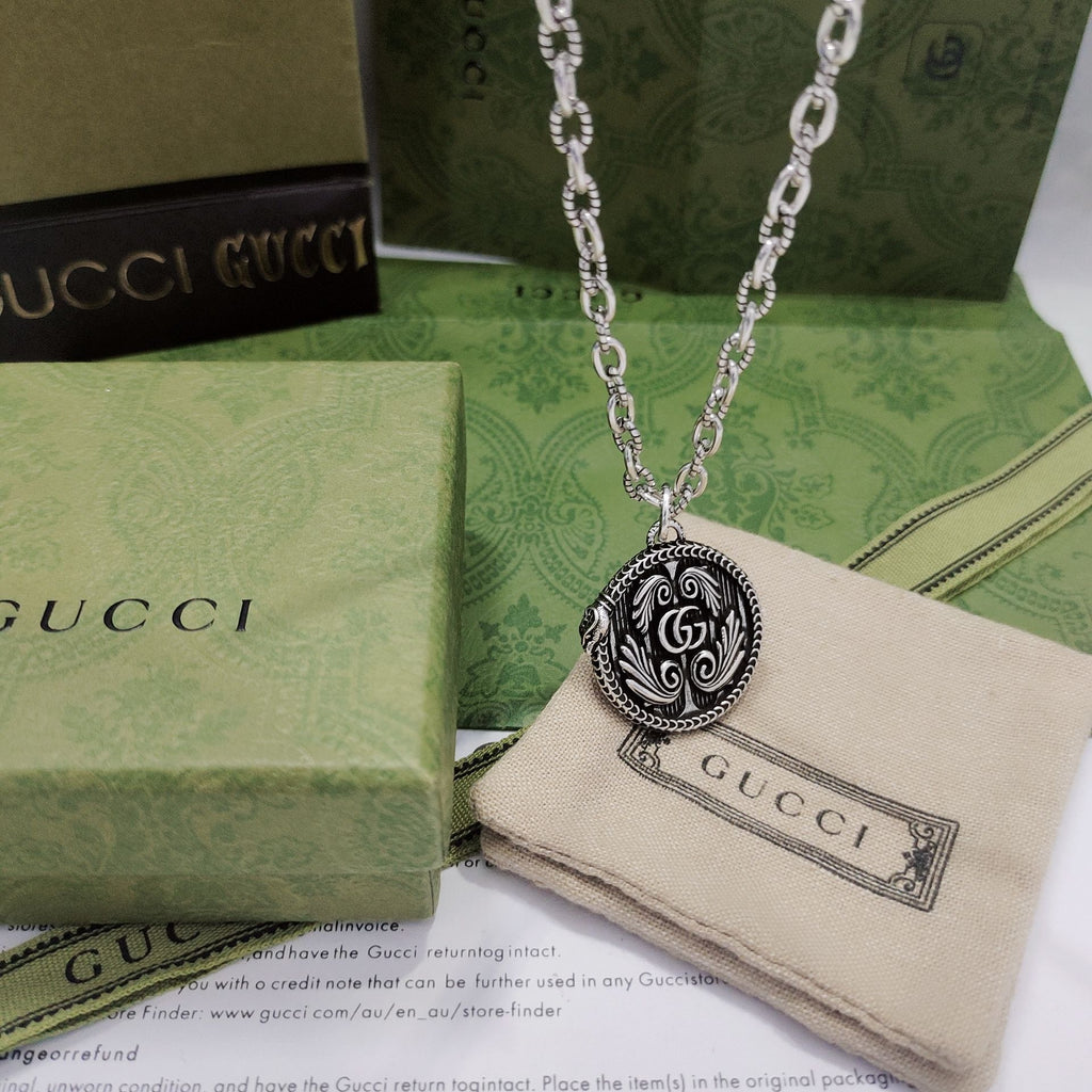 Silver-tone pendant necklace with round logo medallion and engraved swirl pattern