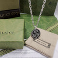 Silver-tone pendant necklace with round logo medallion and engraved swirl pattern