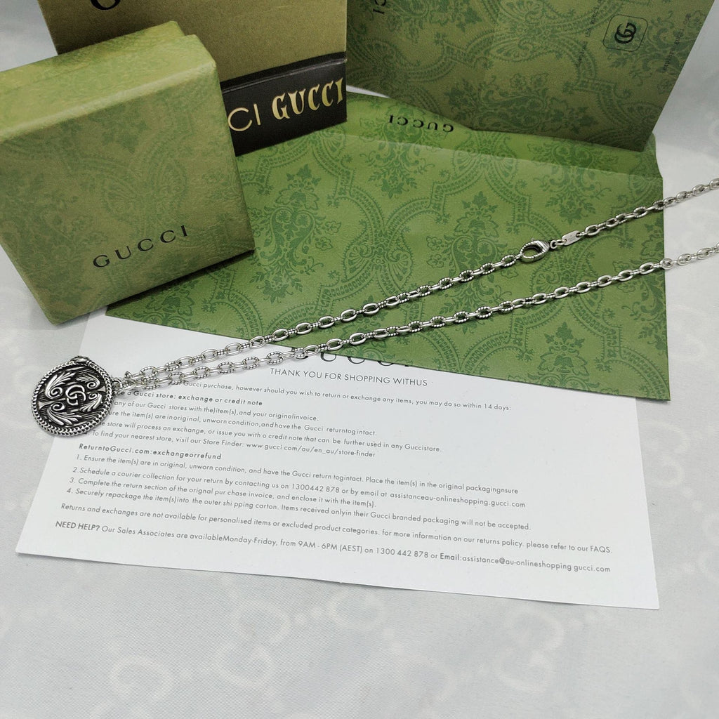 Silver-tone pendant necklace with round logo medallion on a long chain