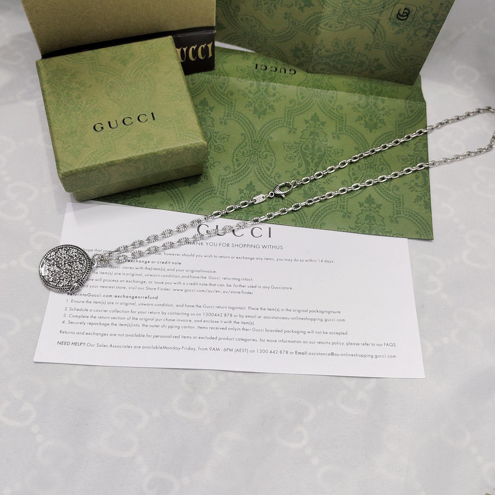 Silver-tone round logo pendant necklace with ornate engraved border and chain