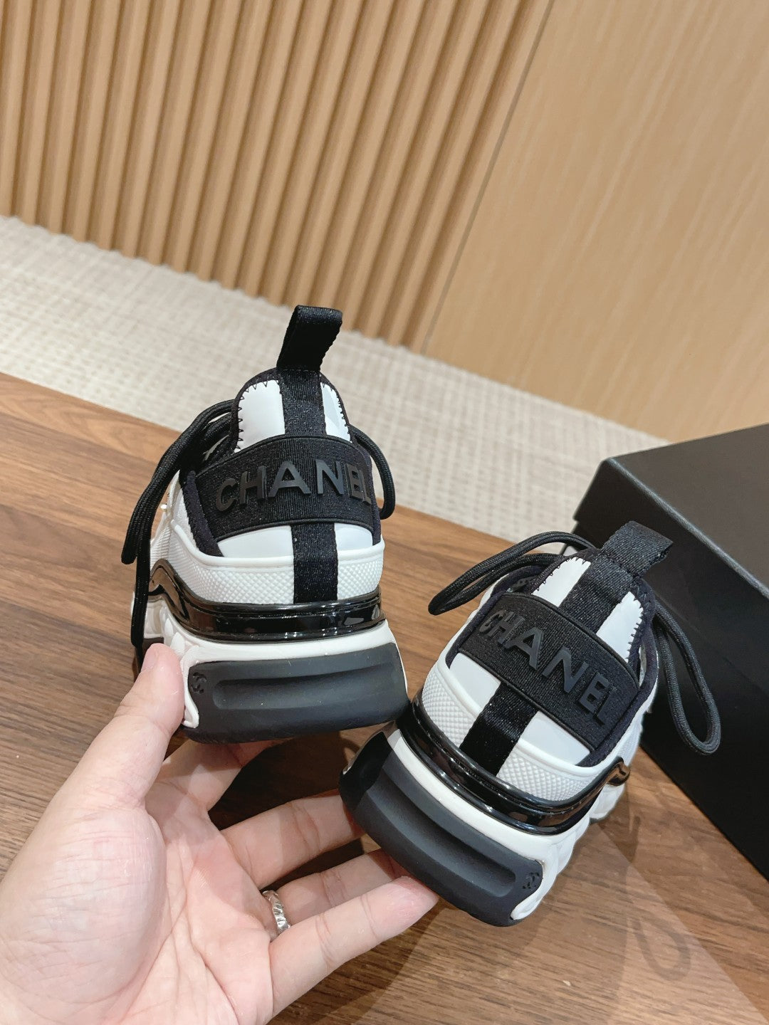 Back view of white and black unisex sneakers with CHANEL logo on heel