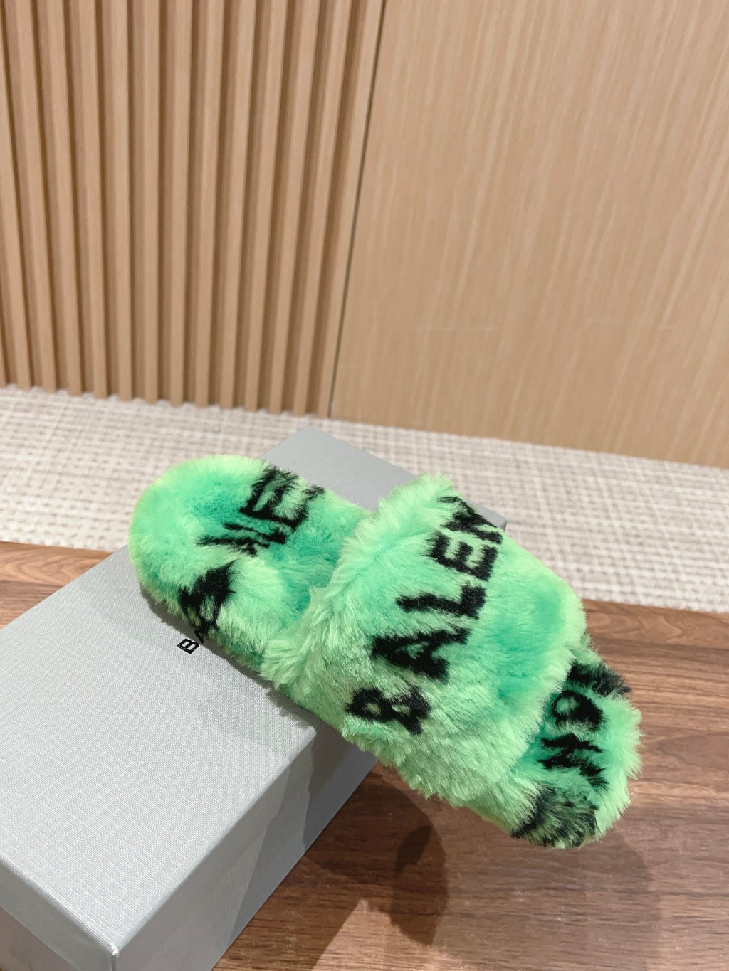 Mint green faux-fur slide sandal with black lettering on white shoebox, angled view.
