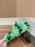 Mint green faux-fur slide sandal with black lettering held near shoebox.