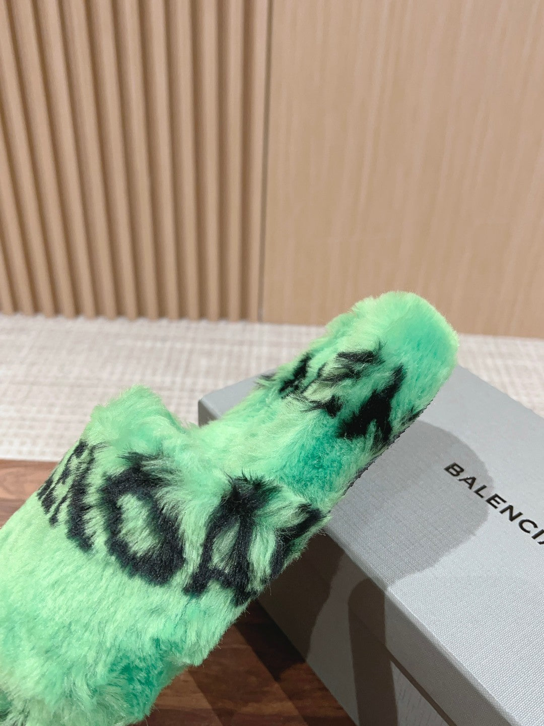 Mint green faux-fur slide sandal with black lettering, single pair resting on box.