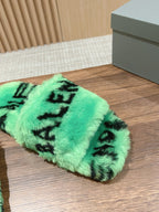 Mint green faux-fur slide sandal with black lettering, sole facing down on wood floor.