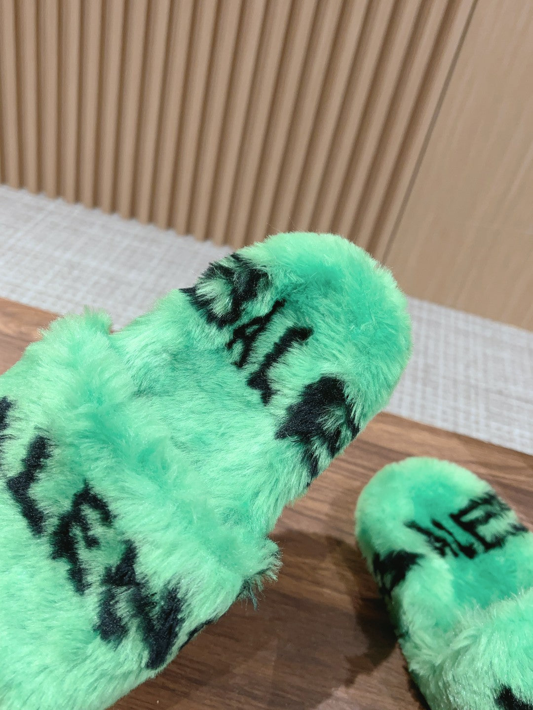 Mint green faux-fur slide sandal with black lettering, close-up of upper strap.