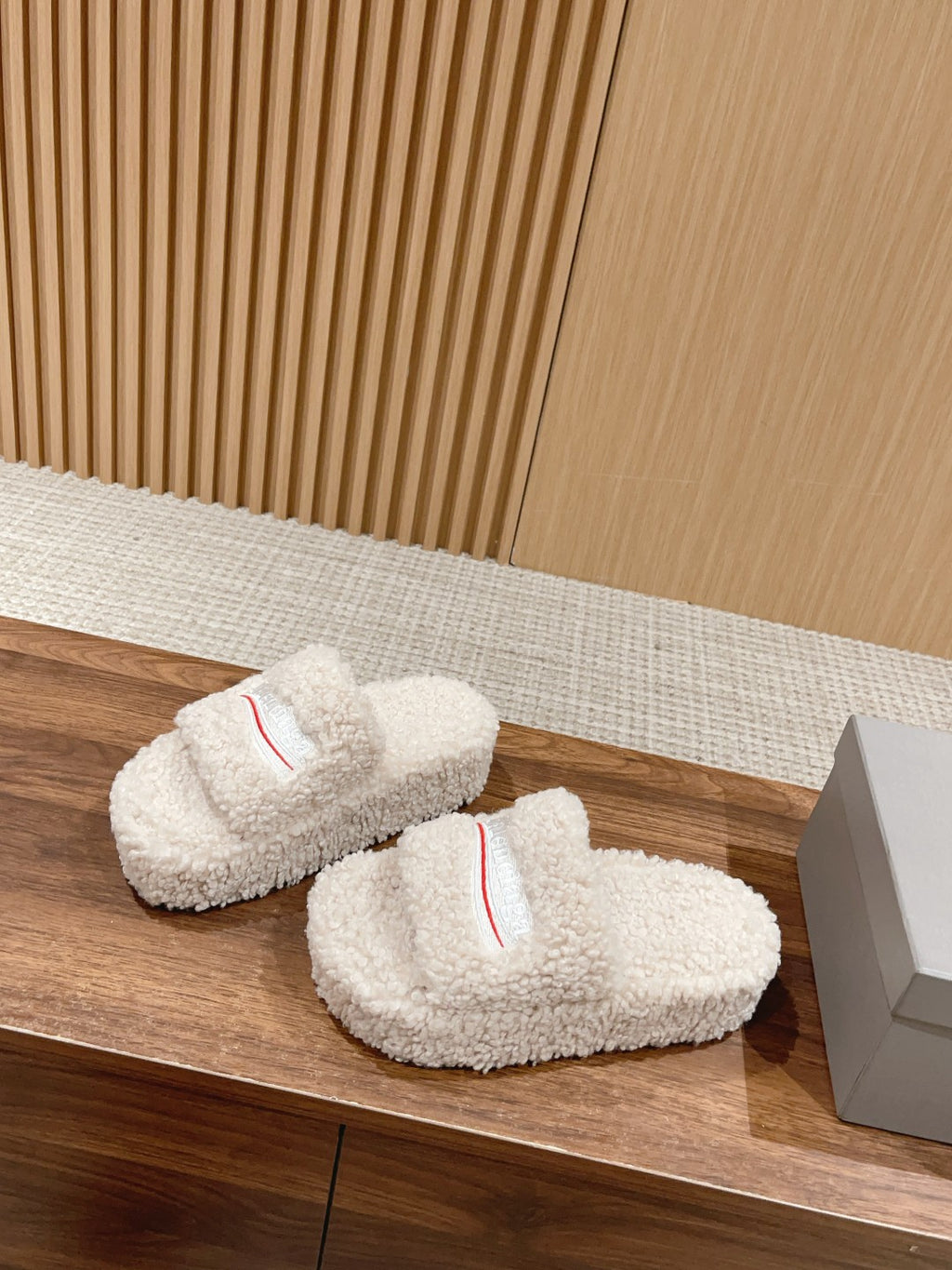 Pair of white shearling slide sandals with red logo stripe on the front