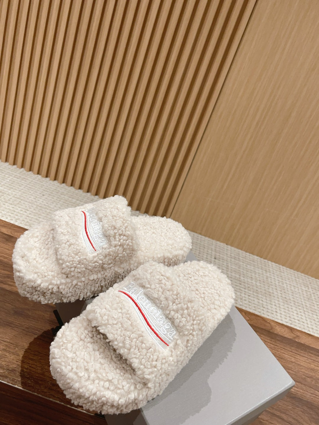 Two white shearling slide sandals with red logo stripe on the top strap