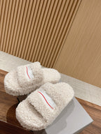 Two white shearling slide sandals with red logo stripe on the top strap