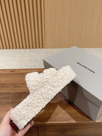 White teddy slide sandals held near a Balenciaga box, with red logo stripe