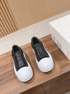 Pair of black sneakers with white soles and black upper laced with eyelets