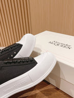 Black sneakers with white rubber sole, studded side strip, laid beside box