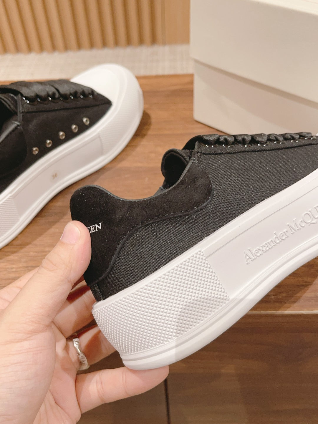 Black sneakers with white rubber sole; hand-held shoe with Alexander McQueen logo
