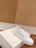 White lace-up sneaker on box, with perforated toe panel and flat rubber sole