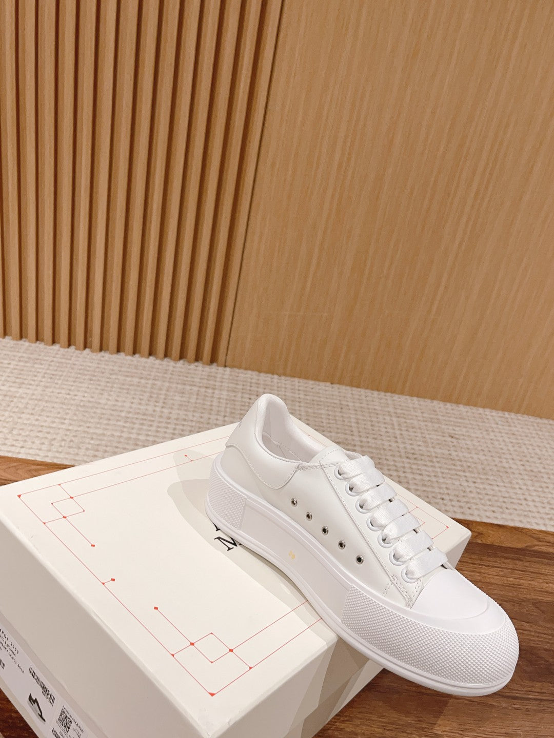White lace-up sneaker on box, with perforated toe panel and flat rubber sole