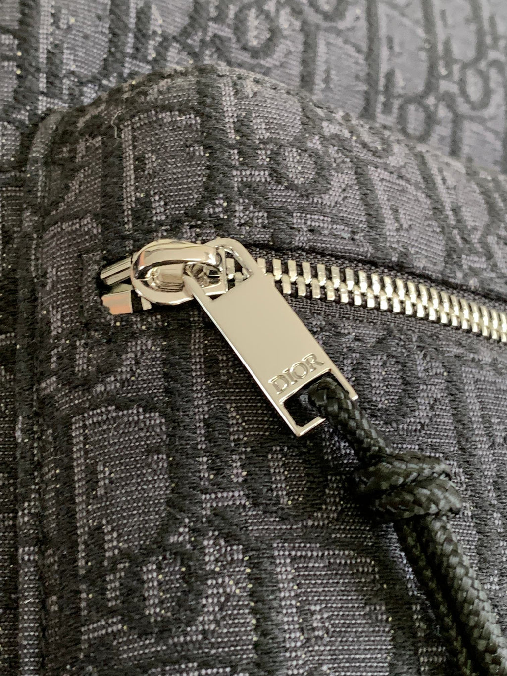 Dior men's monogram backpack close-up of zipper pull with Dior logo tag