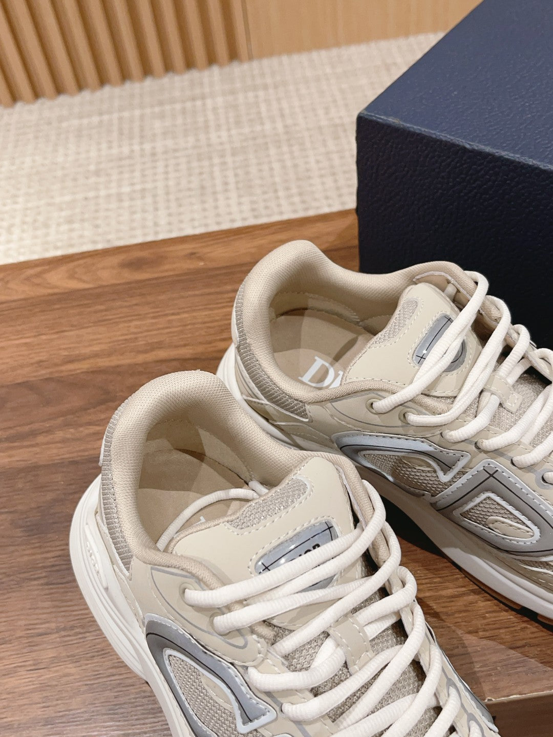 Dior unisex sneakers close-up showing light beige uppers, gray logo, and white laces