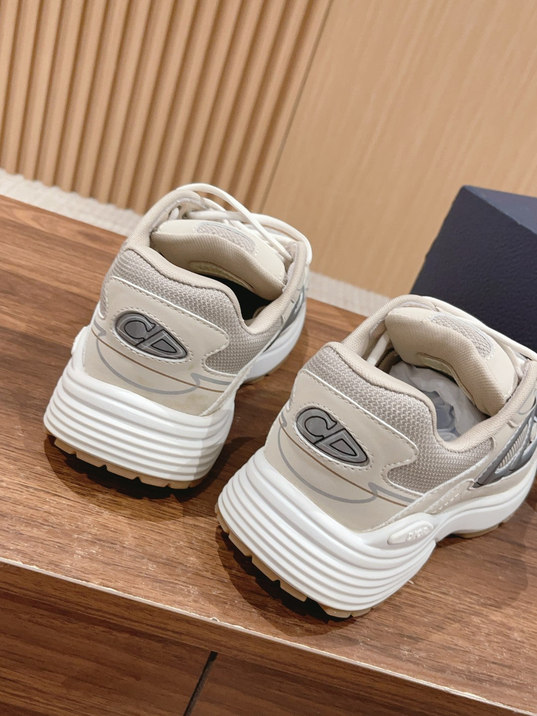 Dior unisex sneakers back view with light beige uppers, gray emblem, and striped sole