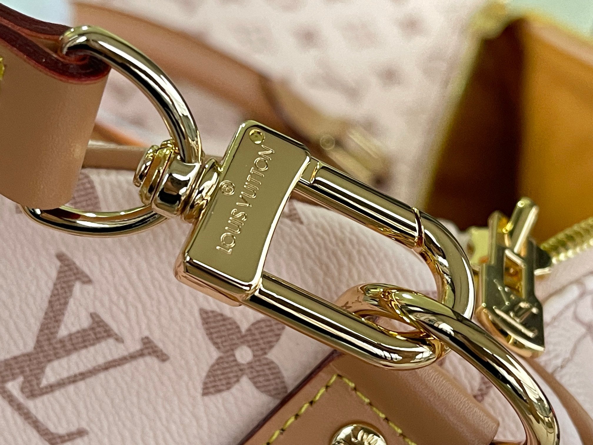Gold-tone key ring clasp on tan-and-pink monogram bag strap
