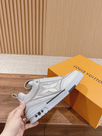 White Louis Vuitton leather sneakers held in hand, lace-up front with logo detail
