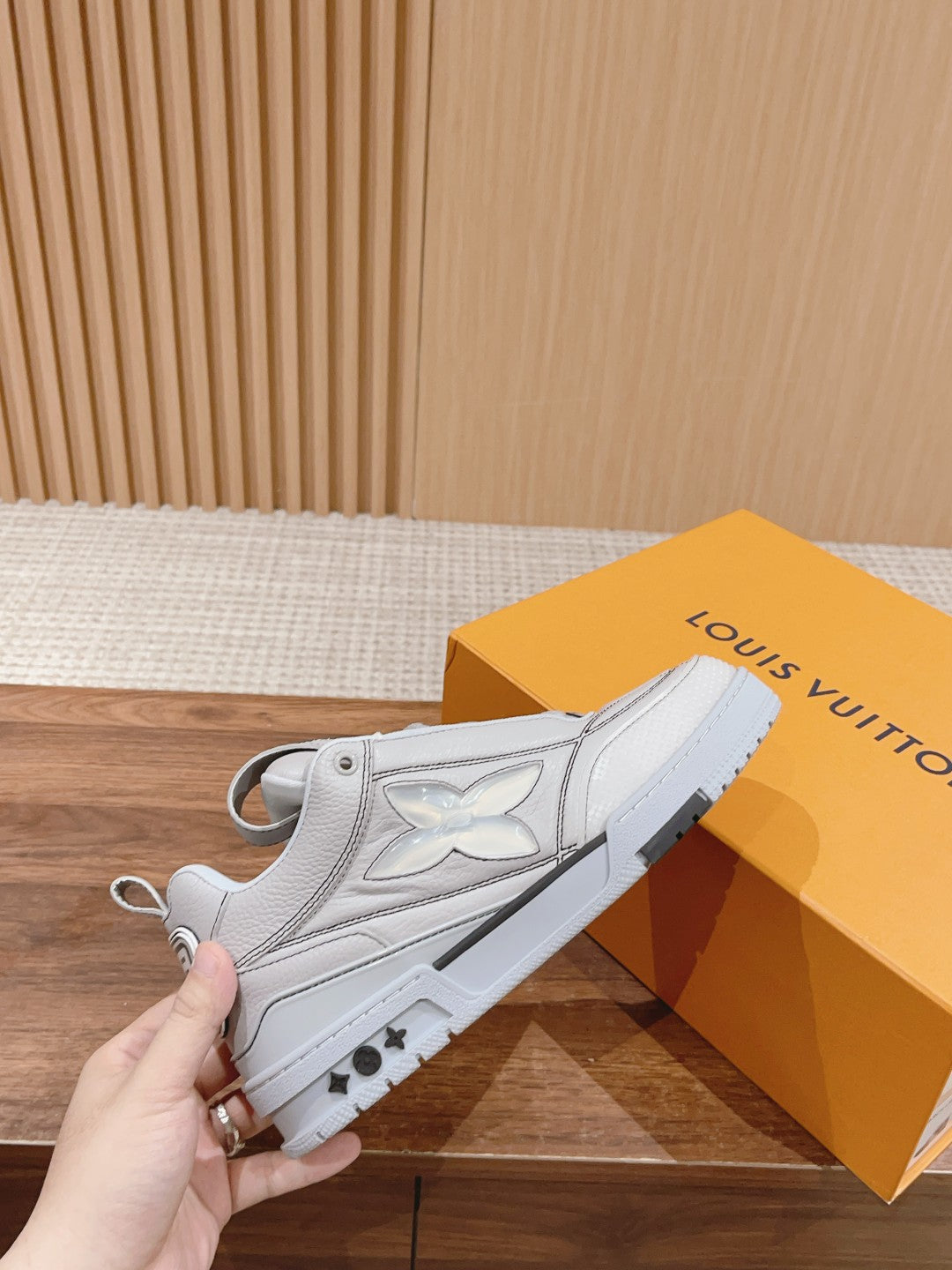 White Louis Vuitton leather sneakers held in hand, lace-up front with logo detail