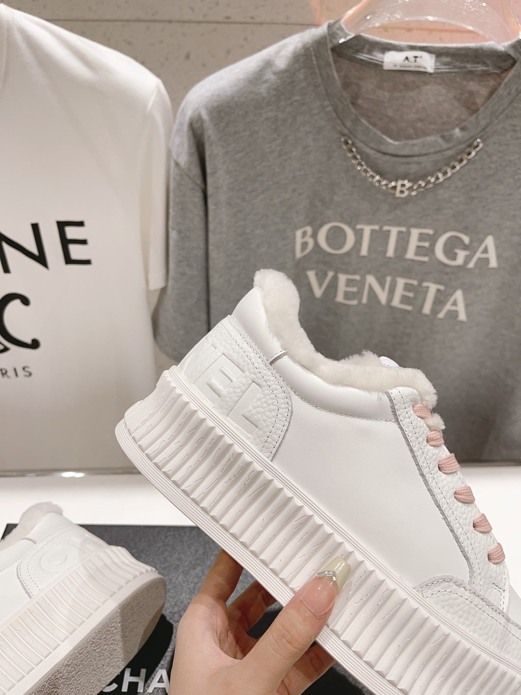 Chanel white sneaker held up, showing pink laces and thick textured platform sole