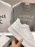 Chanel white sneaker held up, showing pink laces and thick textured platform sole