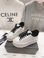 Women’s Chanel luxury sneakers, white with black laces and fuzzy collar on a shoebox