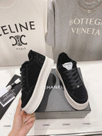 Black suede lace-up sneakers with white ridged sole and Chanel logo patch on tongue