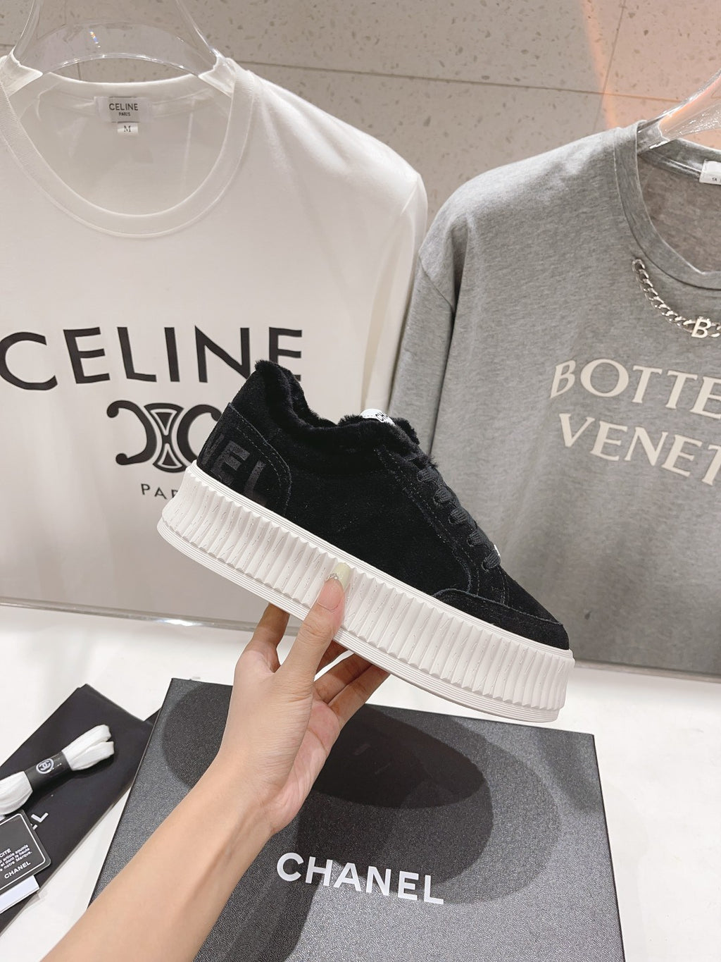 Single black lace-up sneaker with white ridged sole, held above a Chanel box