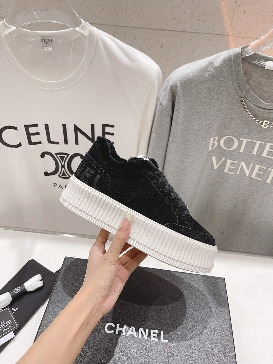 Single black lace-up sneaker with white ridged sole, held above a Chanel box