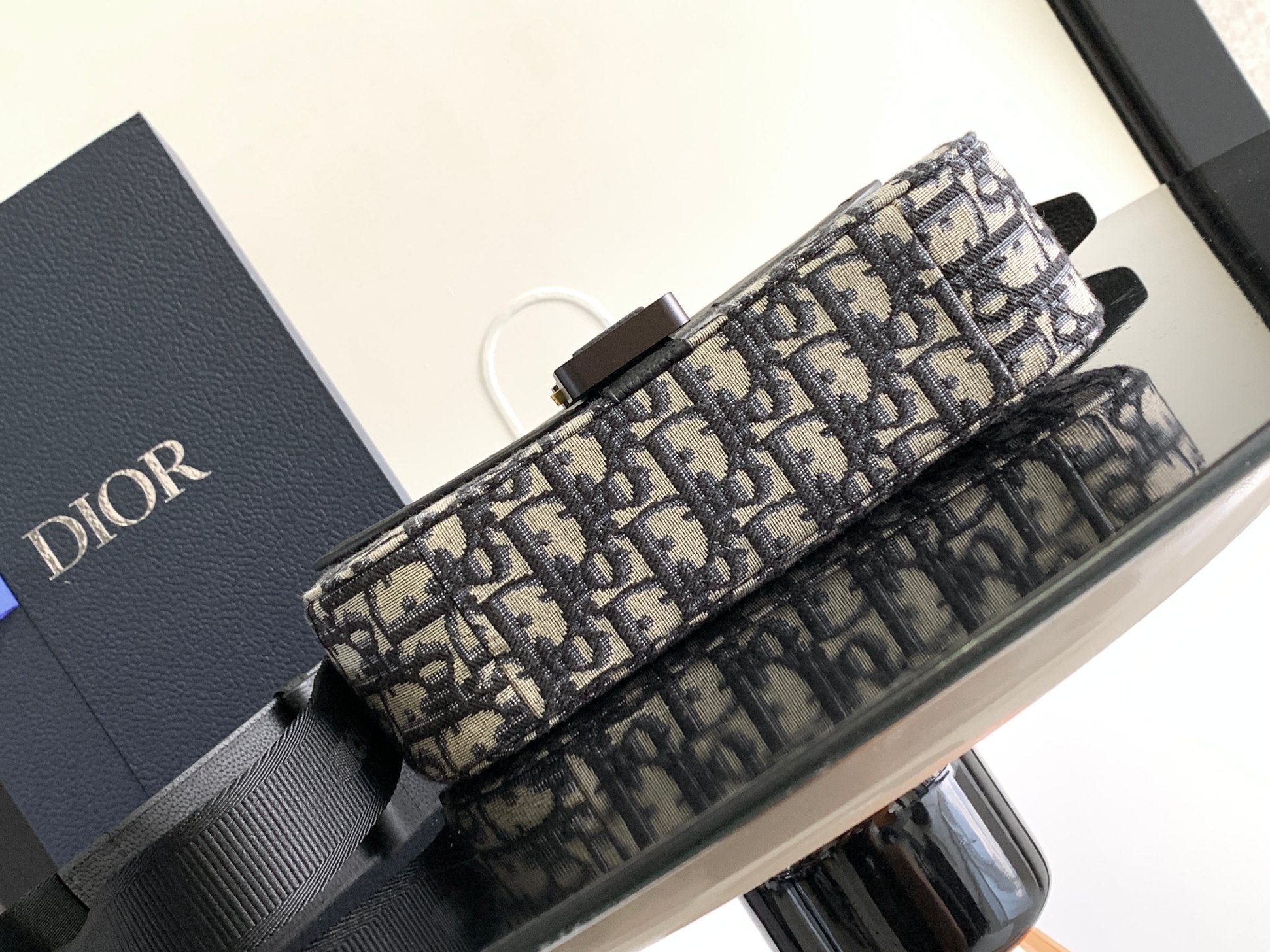 Dior bag showing Dior monogram canvas strap attachment and black leather handles