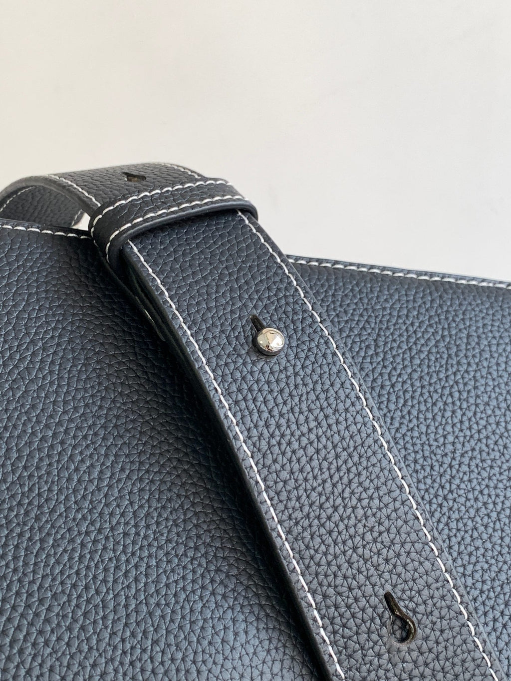Dark textured leather bag corner with stitched edge and small metal snap