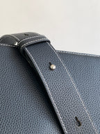 Dark textured leather bag corner with stitched edge and small metal snap