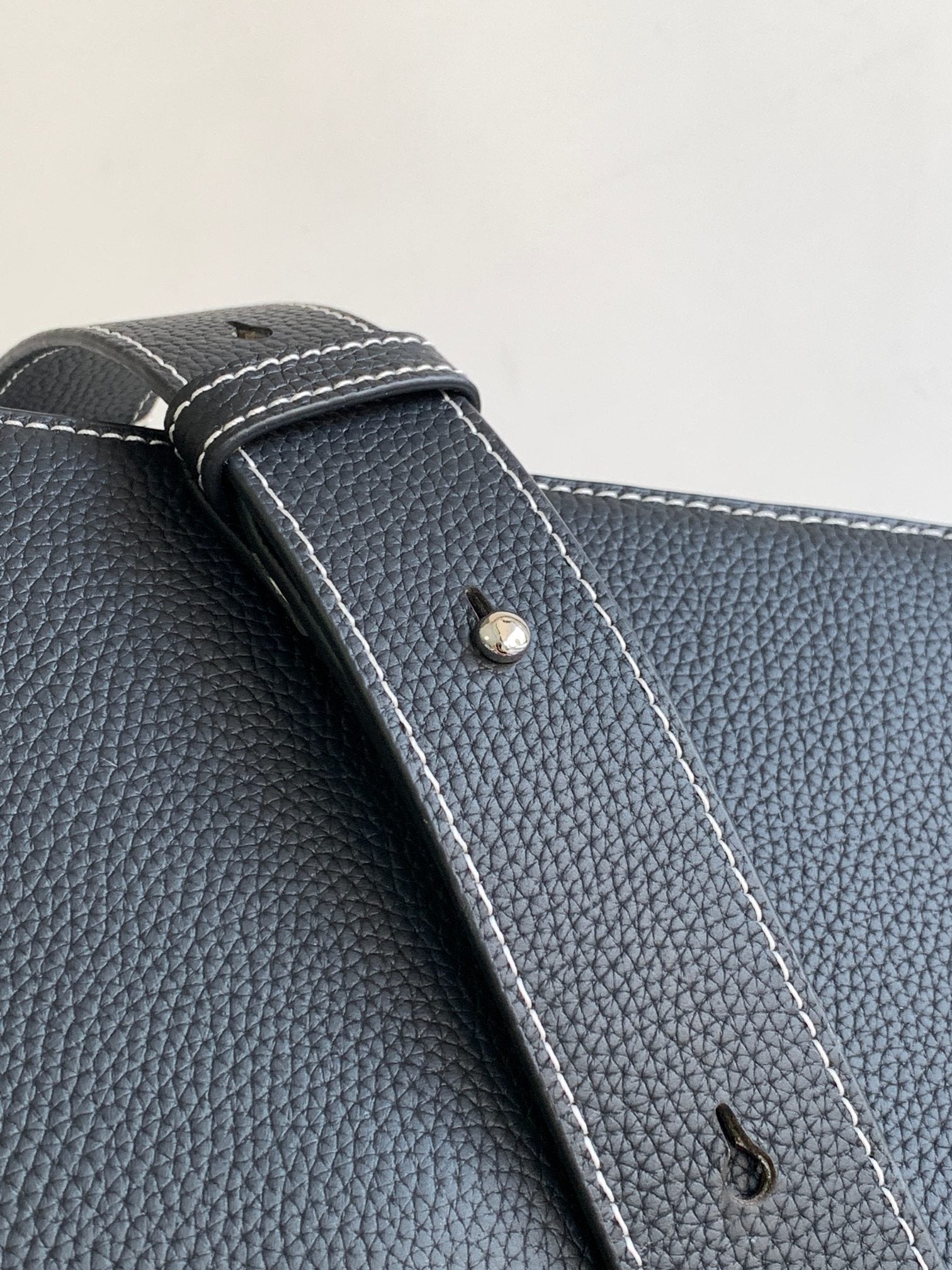Dark textured leather bag corner with stitched edge and small metal snap
