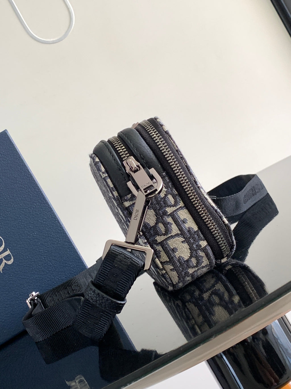 Crossbody bag with navy and beige Dior pattern fabric, zip closure, and adjustable strap