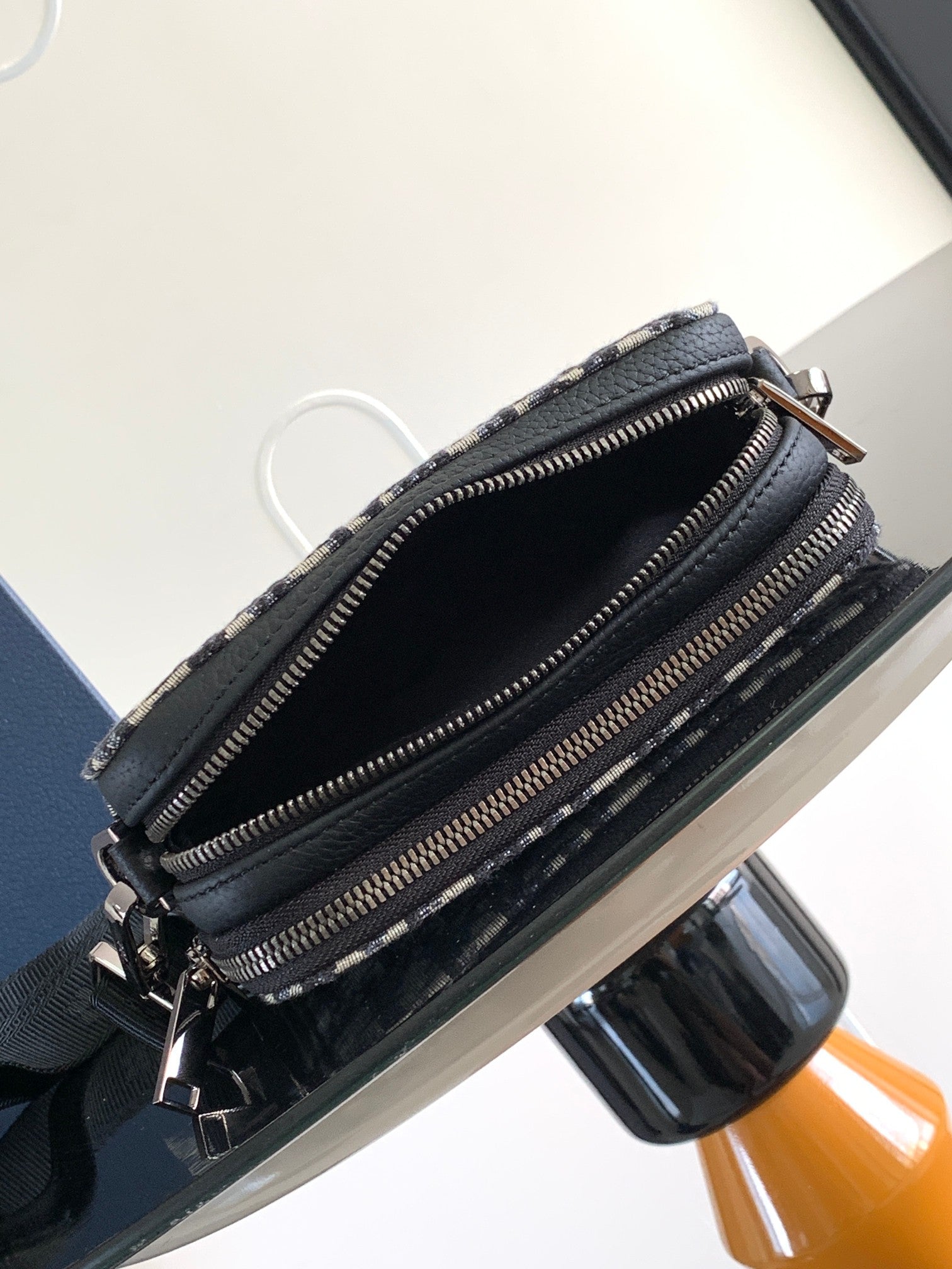 Crossbody bag open view with black interior, zip pockets, and navy/beige patterned exterior
