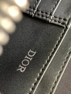 Leather bag panel close-up with “Dior” embossing and stitched edge in dark color