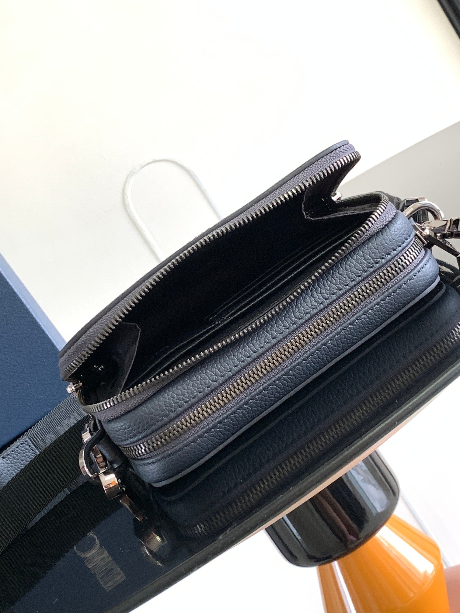 Navy leather crossbody bag with open top, black lining, and two gold-tone zippers
