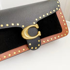 Coah Bags handbag flap detail, textured black panel with brown trim, gold studs and clasp.