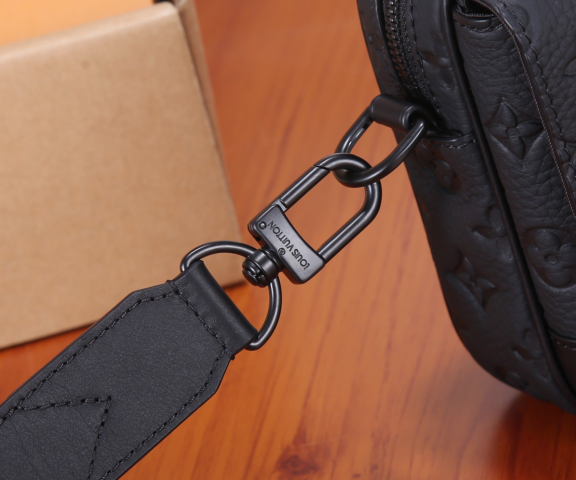 Close-up of dark crossbody bag strap with metal rings and branded connector